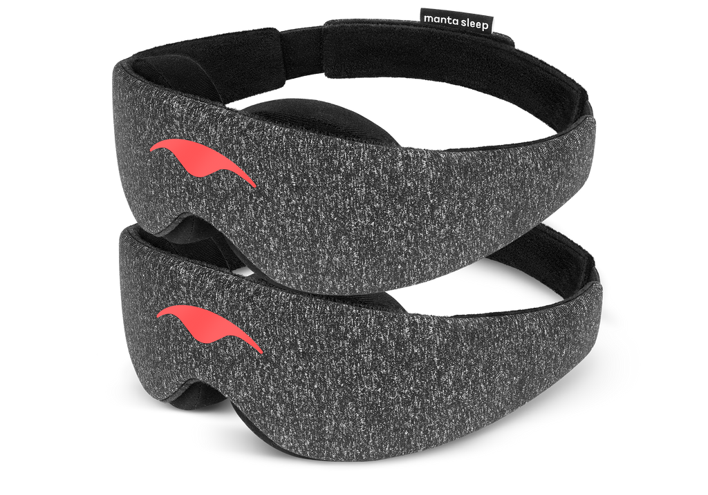 Two Carbon Black Manta Sleep Masks are stacked vertically, isolated on a white background. Each mask highlights its speckled, dark gray heathered fabric exterior, a bright coral-red Manta Sleep logo printed on the front center, and a soft black interior lining with a small brand label attached to the top strap.