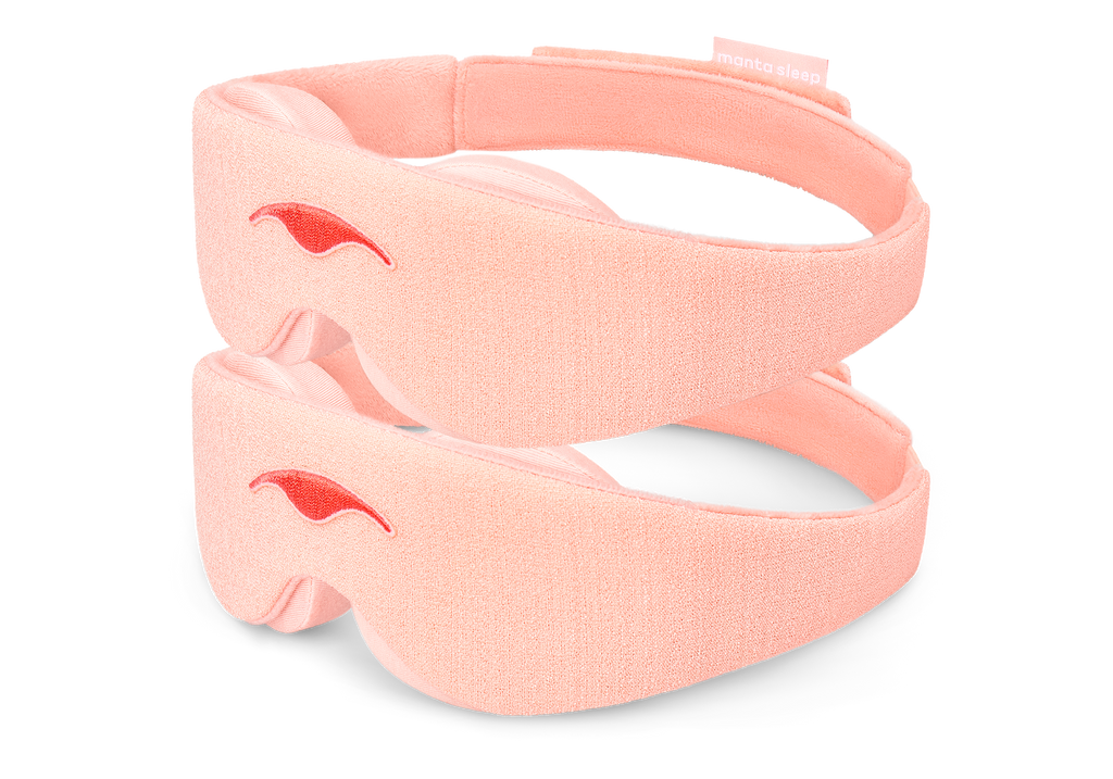Two Sunrise Pink Manta Sleep Masks are stacked vertically, isolated on a pure white background. Each mask displays its textured light pink exterior fabric, a centered darker pink embroidered Manta Sleep logo, and a glimpse of the plush, contoured interior eye padding.