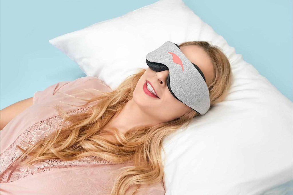 Person lying down on a fluffy white pillow, smiling while wearing a heather grey Manta Sleep Mask Classic.