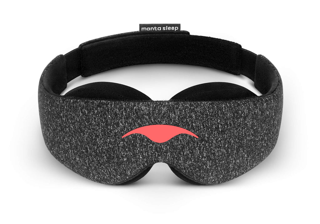 Front view of the Carbon Black Manta Sleep Mask arranged in a freestanding circle on a white surface. The mask features a dark gray speckled heather texture with the coral-red Manta Sleep logo on the front and a black brand label at the rear.