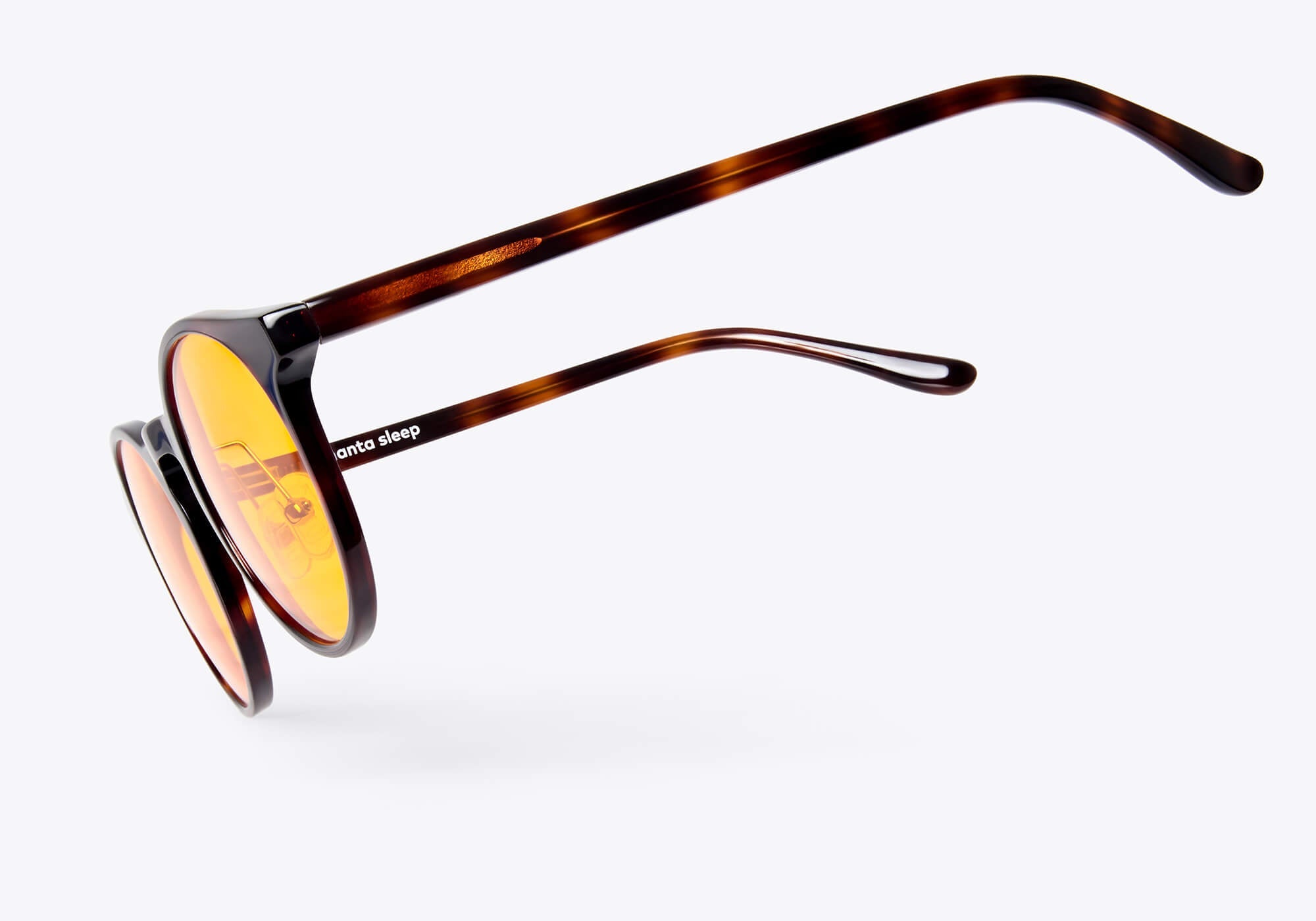 Side-angle floating view of round tortoiseshell glasses with yellow lenses, displaying the slim temple arm with a white Manta Sleep logo.
