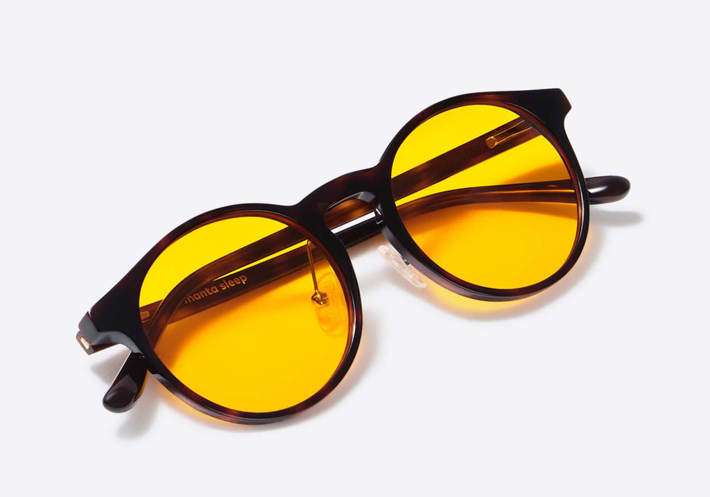 High-angle close-up shot of round tortoiseshell glasses featuring vibrant yellow lenses, with white text "manta sleep" printed on the inner temple.