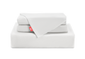 A neat stack of folded white Manta Arctic sheets and pillowcases, featuring a bright red Manta Sleep logo tab, isolated on a white background.