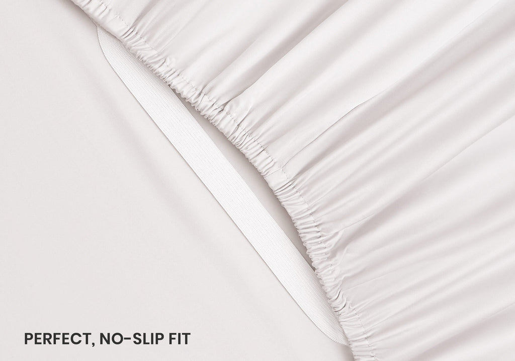 Close-up shot of an elastic corner strap on a white fitted sheet, with text overlay "Perfect, no-slip fit".