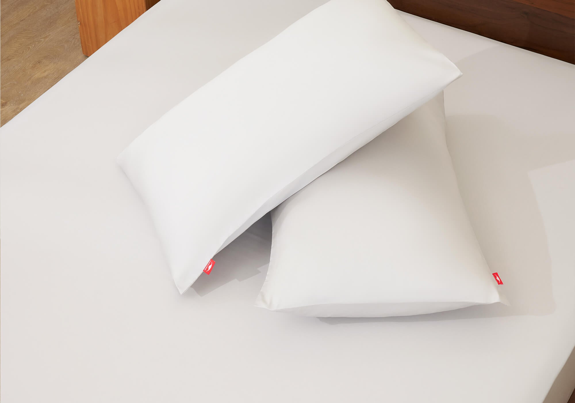 High-angle view of two white Manta Sleep pillowcases with red logo tags stacked crosswise on a white fitted sheet.