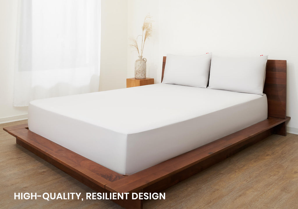 Studio wide shot of a minimal dark wooden platform bed neatly made with a white Manta Arctic Bedsheet Set. Text overlay: "High-quality, resilient design".