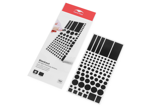 High-angle shot of a Manta Sleep Blackout sticker pack next to an open sheet filled with one hundred black light blocking stickers of different sizes.