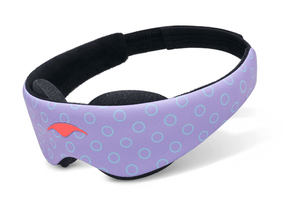 An angled product shot of the Manta KIDS Sleep Mask floating against a plain white surface. The exterior band displays a playful purple design with light blue circle outlines and a small orange emblem on the front left. The inner side reveals a soft black plush lining and a matching black elastic strap.