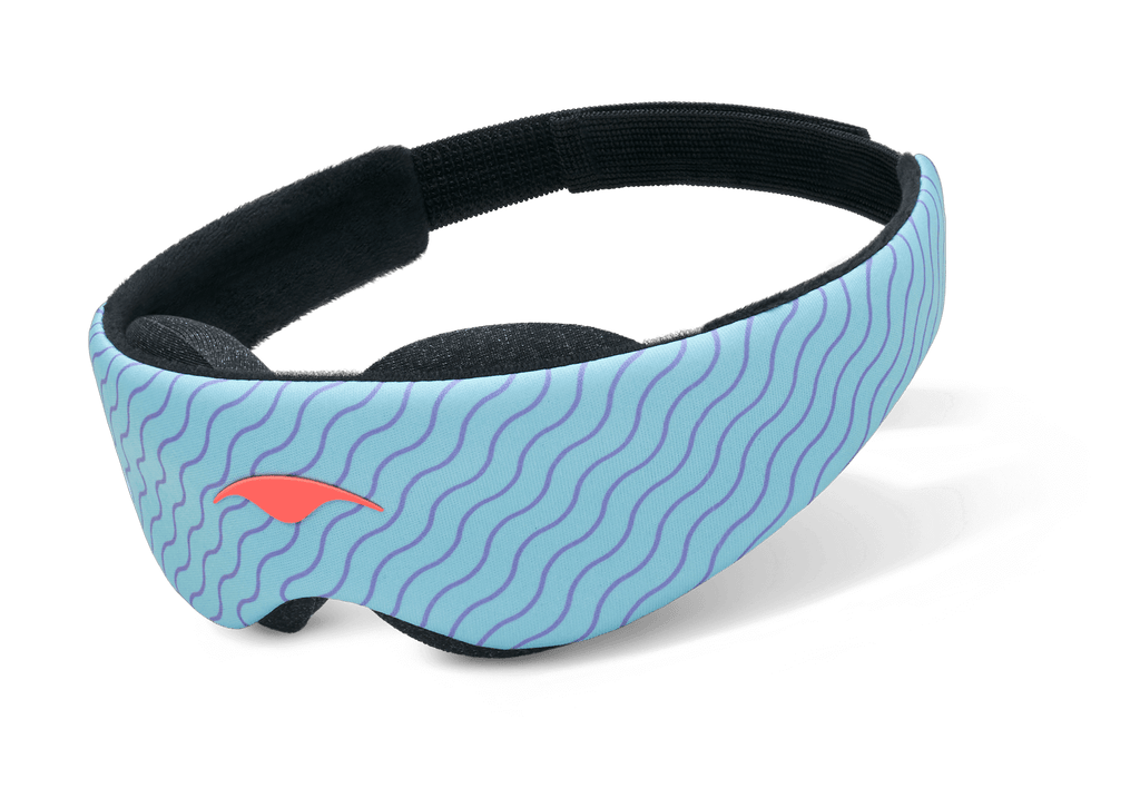 An angled product shot of the Manta KIDS Sleep Mask floating against a plain white surface. The exterior band displays a light blue design with thin purple wavy lines and a small orange emblem on the front left profile. The inner lining features soft black plush eye cups and a black elastic strap.