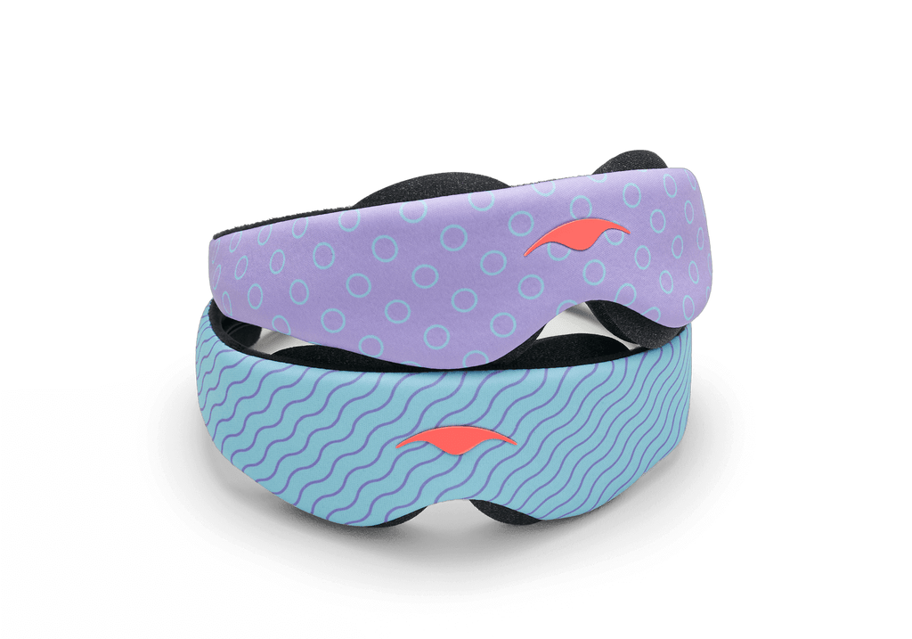 Two variants of the Manta KIDS Sleep Mask stacked on top of each other against a white background. The top mask displays a purple pattern with light blue circle outlines, while the bottom mask features a light blue pattern with dark blue wavy lines. Both masks are finished with a central orange Manta Sleep logo.