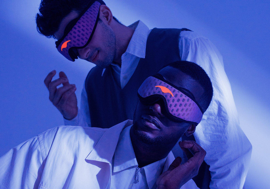 Two men under a cool blue light wearing purple Manta Sleep Mask PROs over their eyes, showcasing the comfortable blackout fit.