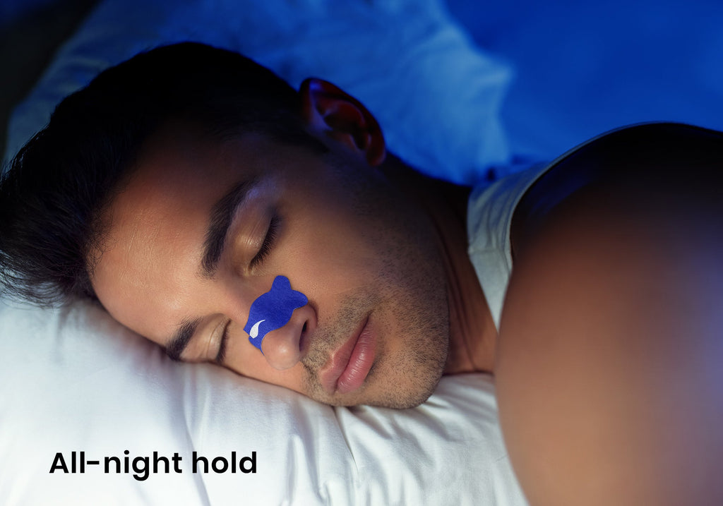 Close-up of a man sleeping with a blue Manta nasal strip on his nose under blue lighting. Text overlay: "All-night hold".