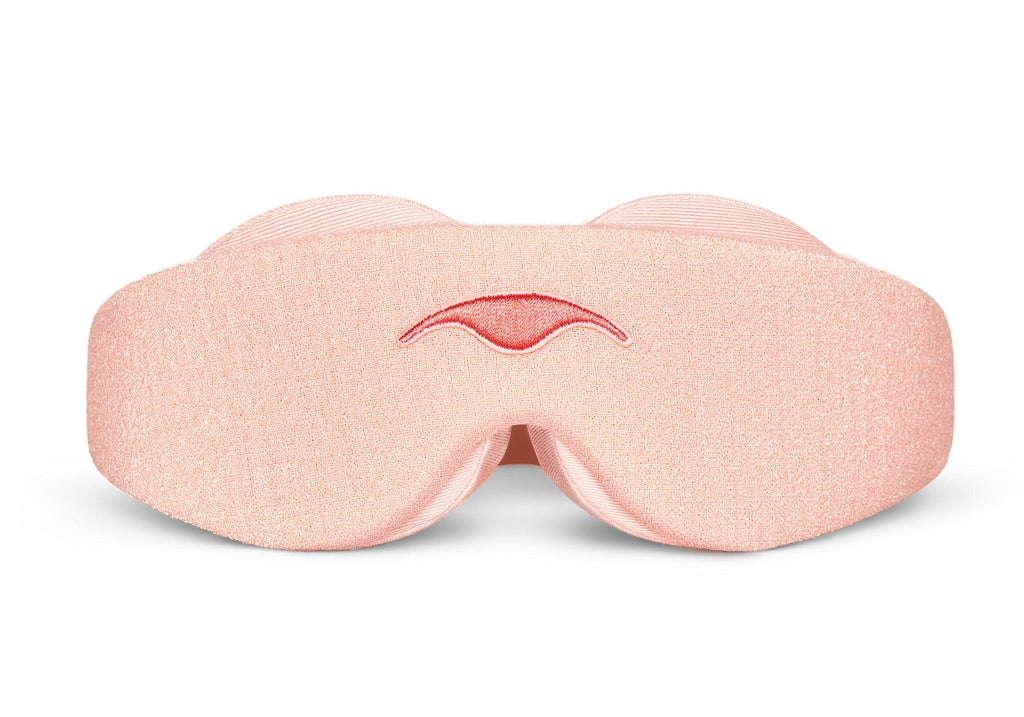 Direct front view of the Sunrise Pink Manta Sleep Mask laid flat against a white backdrop, showing its contoured shape, light pink fabric texture, and a centered, embroidered pink Manta Sleep logo.