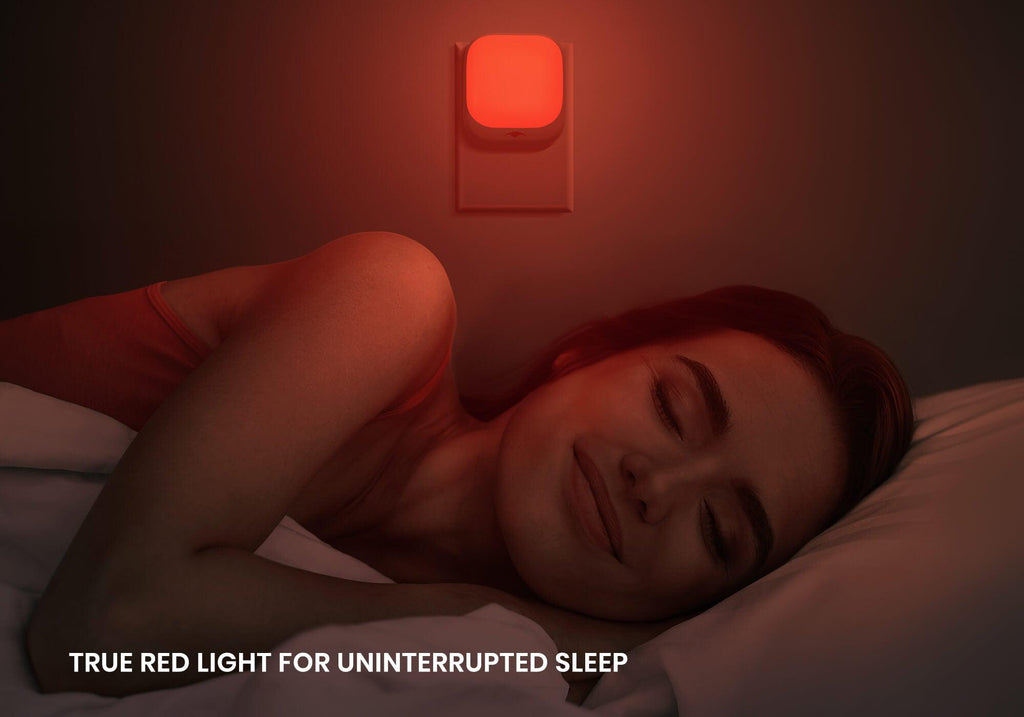 A woman sleeping peacefully in a dark bedroom illuminated by the soft red glow of a wall-mounted Manta Sleep night light.