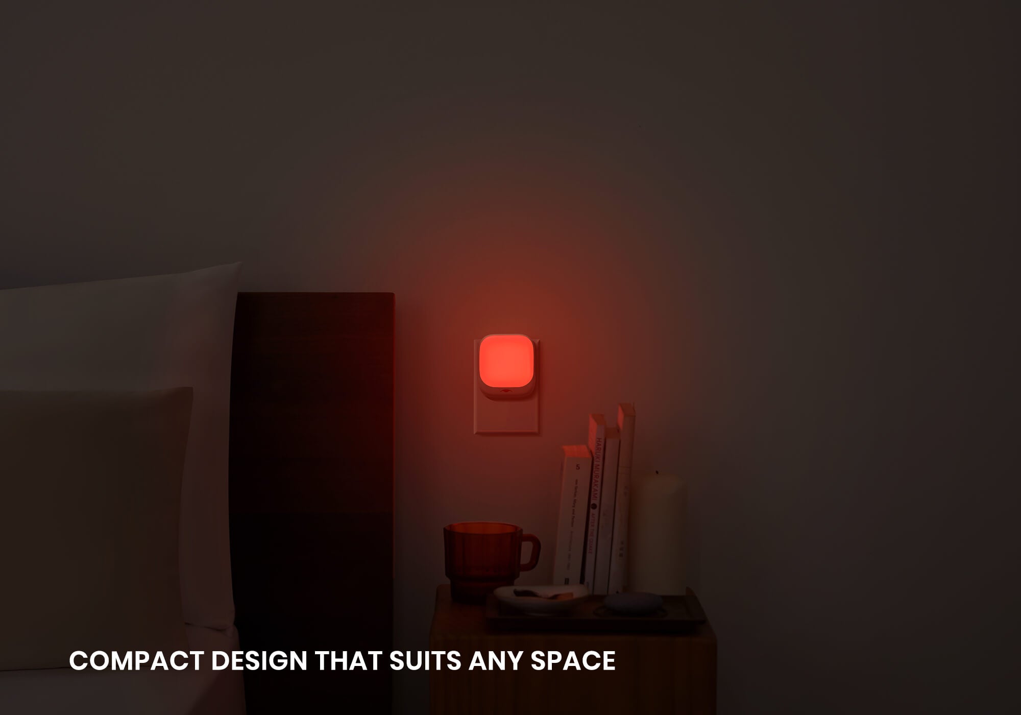 A Manta Sleep night light plugged into a wall outlet, casting a warm red glow next to a dark bedside table.