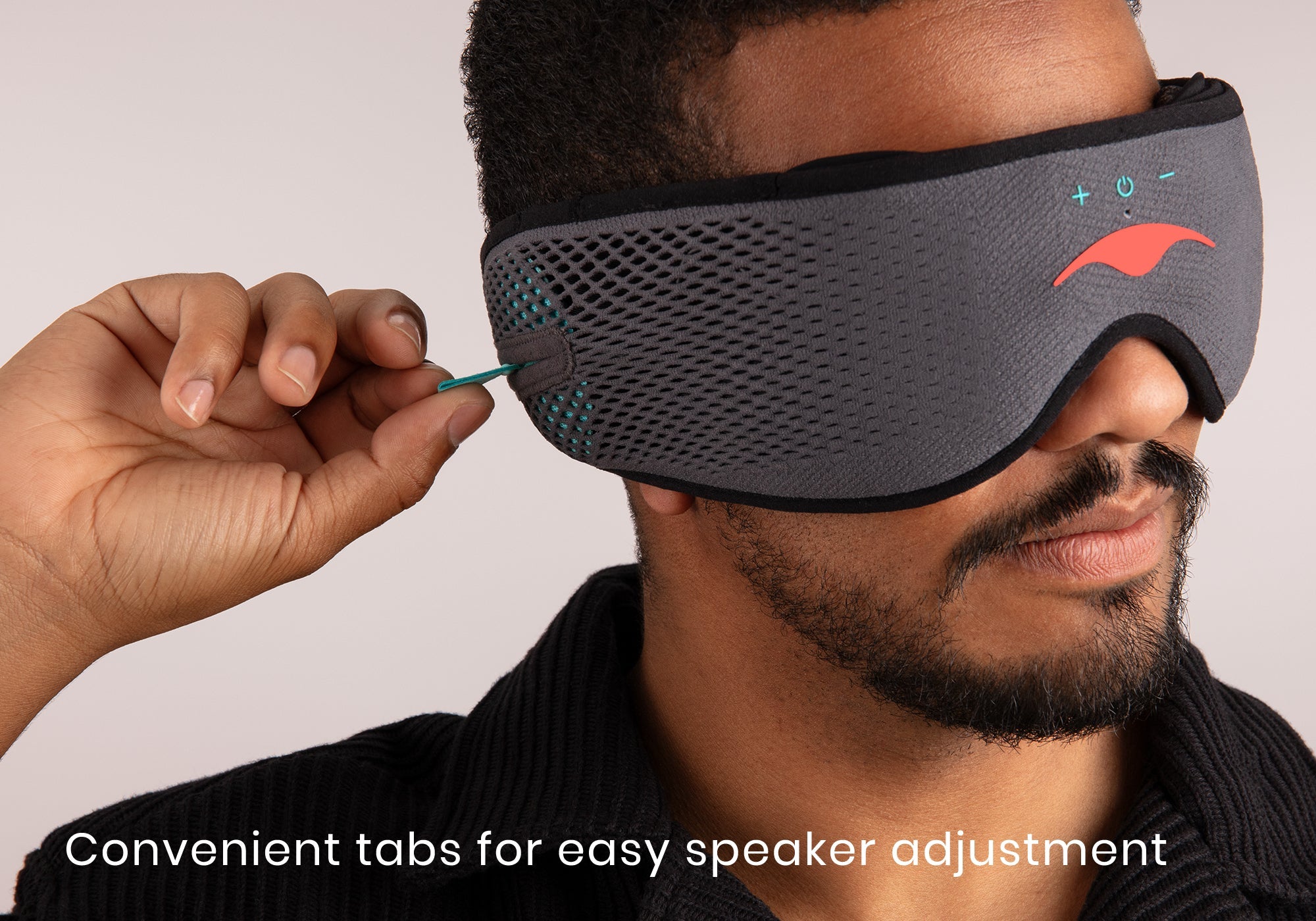 Close-up profile of a man adjusting an ultra-thin speaker tab on his grey mesh sleep mask, captioned "Convenient tabs for easy speaker adjustment".