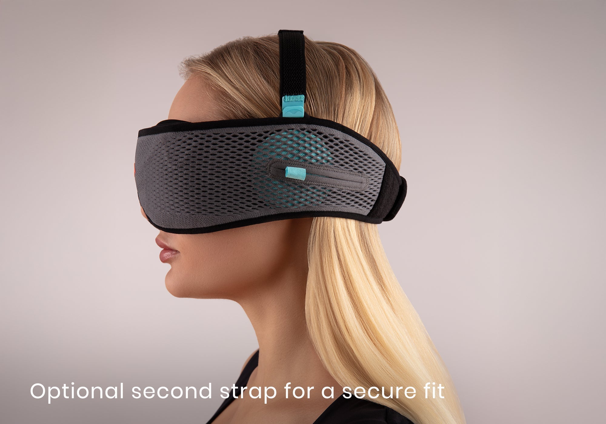 Side profile of a blonde woman wearing a grey mesh sleep mask featuring an adjustable black top strap, captioned "Optional second strap for a secure fit".