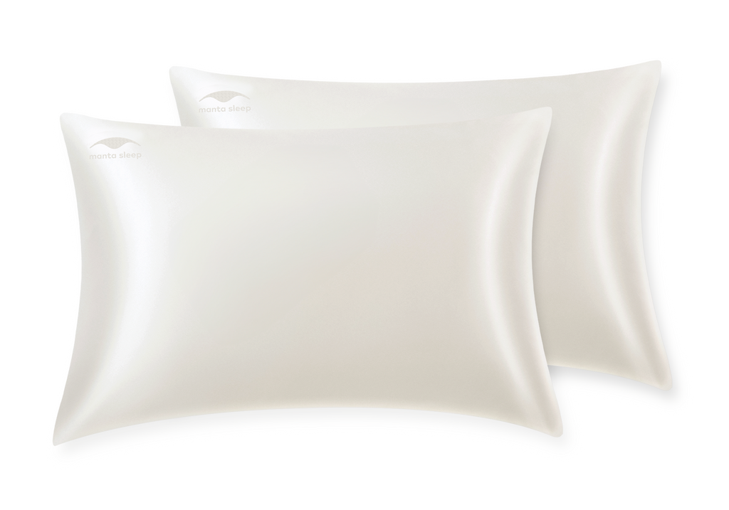 Two pearl white silk Manta Sleep pillowcases overlapping each other, isolated on a clean white background.