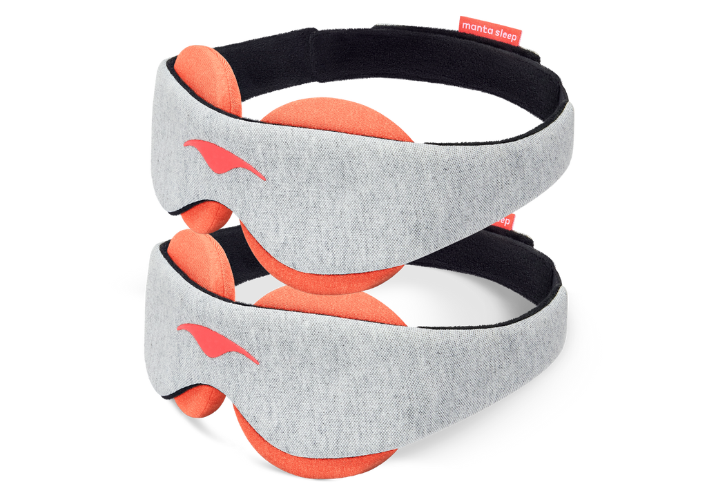 Two identical Manta STEAM Sleep Masks stacked vertically against a solid white background. Both masks feature a light gray heathered jersey knit front band accented by a coral-red Manta Sleep logo on the left side, with thick, circular terracotta-orange heat therapy eye cups visible extending beyond the band.