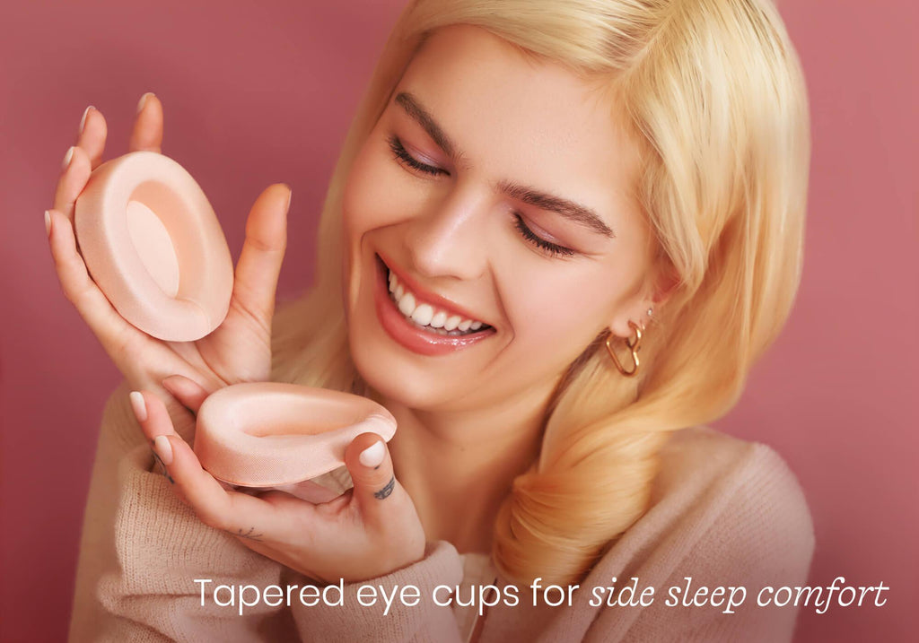 Smiling person holding two contoured pink eye cups. Text overlay reads "Tapered eye cups for side sleep comfort".