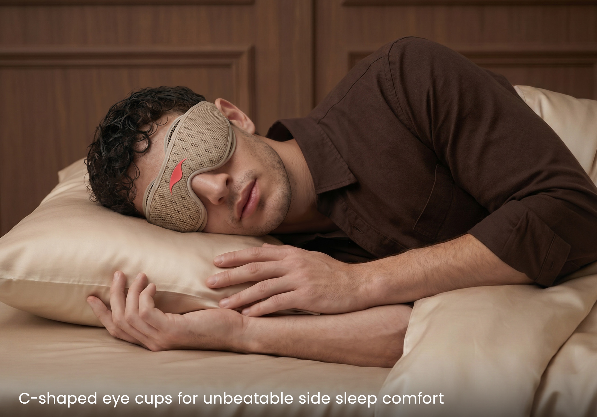 A man sleeping on a bed with a light brown Tranquil Taupe Manta PRO Sleep Mask around his eyes, wearing a brown shirt. Text at the bottom reads "C-shaped eye cups for unbeatable side sleep comfort".
