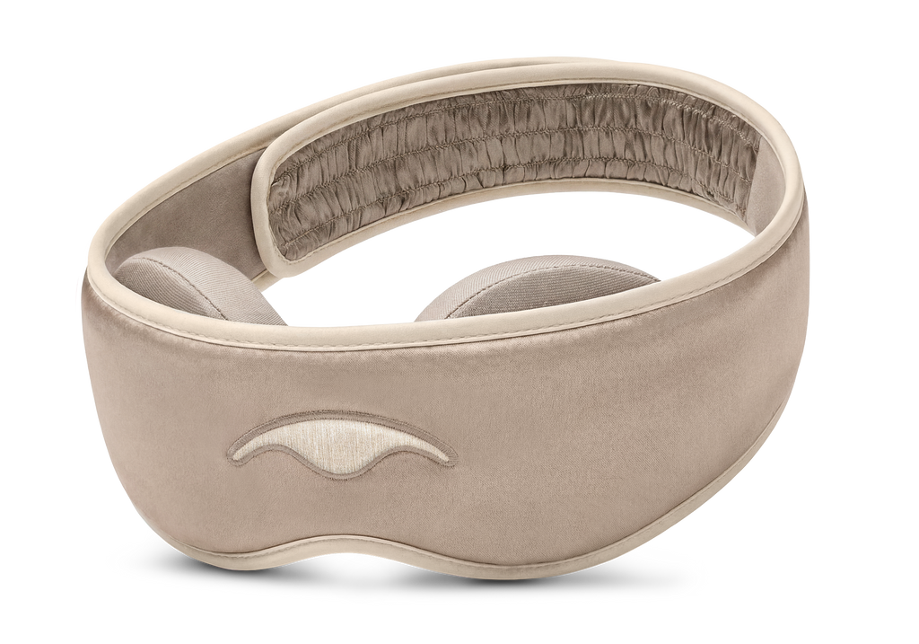 Three-quarter studio shot of the Manta SILK Sleep Mask in Tranquil Taupe, featuring an embroidered beige logo and a ruched back strap section.