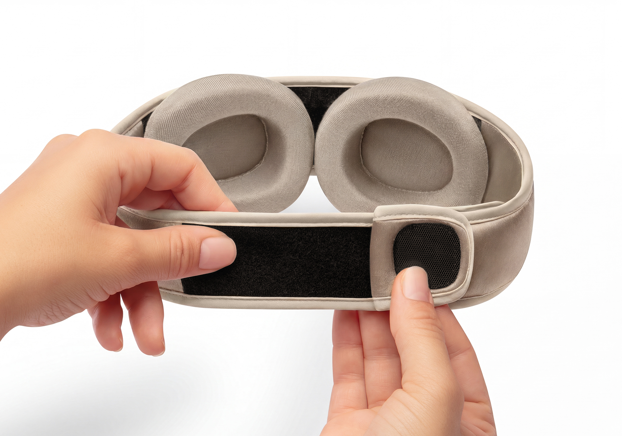 Two hands adjusting the hook-and-loop back closure of a Tranquil Taupe Manta SILK Sleep Mask, revealing two adjustable, padded eye cups.