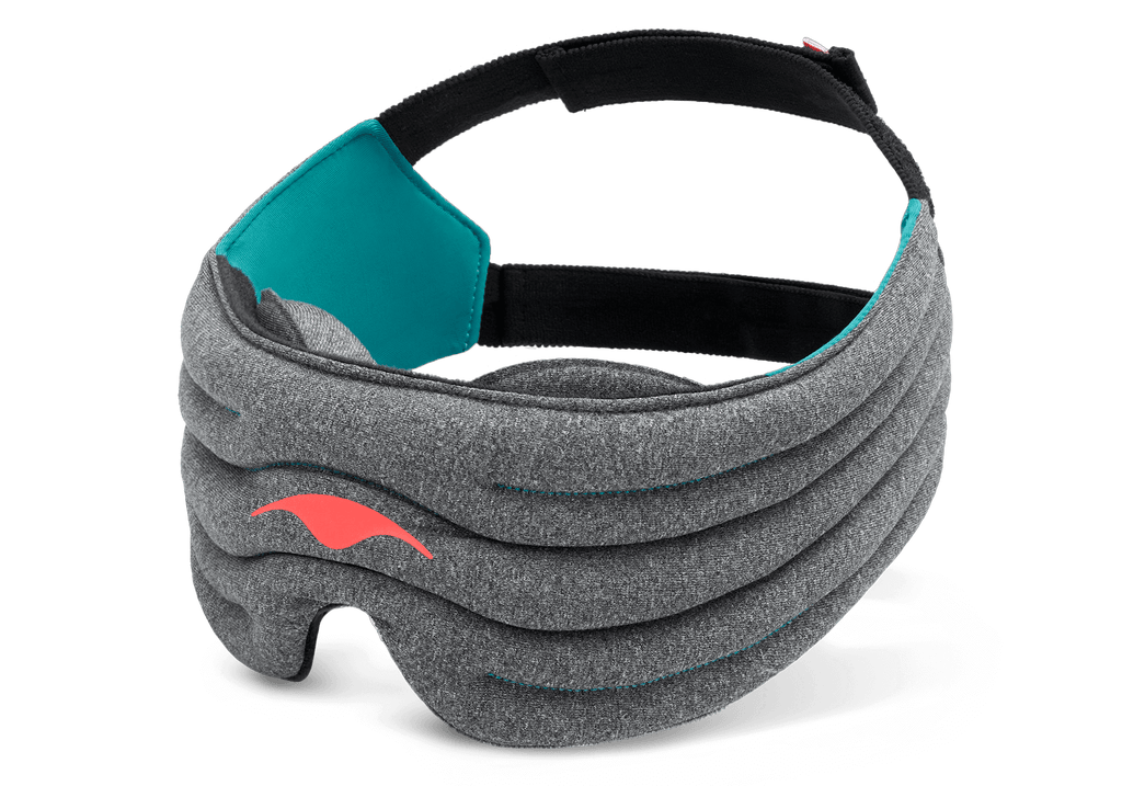 A product shot of the dark heather-gray Manta WEIGHTED Sleep Mask angled against a plain white background. The mask has a segmented, thickly padded front body with a vibrant coral-red Manta ray emblem on the left. The inner lining features a bright teal fabric section on the side panel, transitioning into a wide, adjustable black head strap.