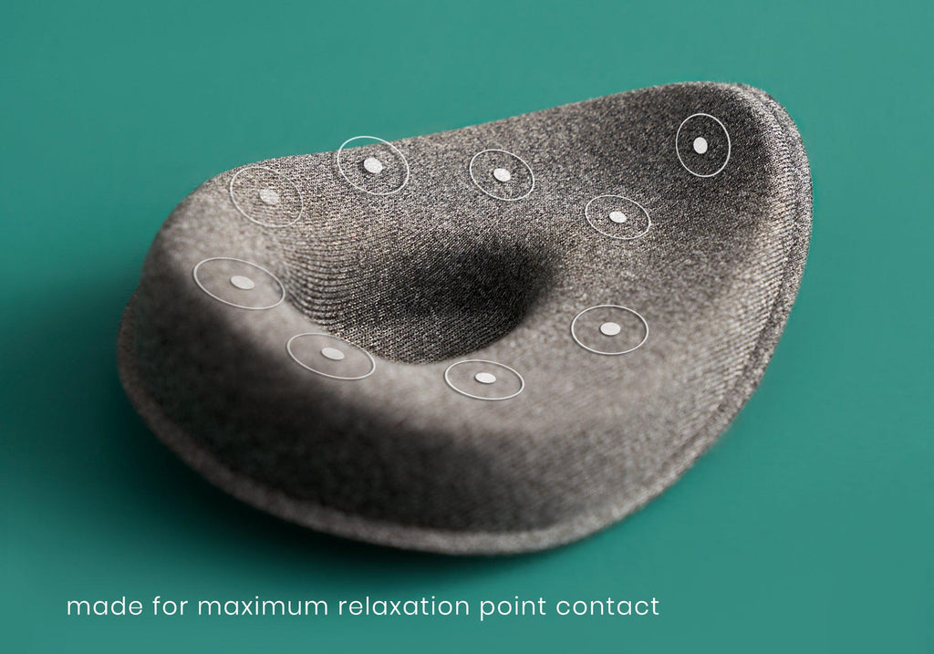 A close-up product feature shot of a single heather-gray modular eye cup resting on a teal surface. Circular graphics with white center dots overlay the cushioned rim of the cup to map out the targeted pressure points. White text at the bottom left reads, "made for maximum relaxation point contact."